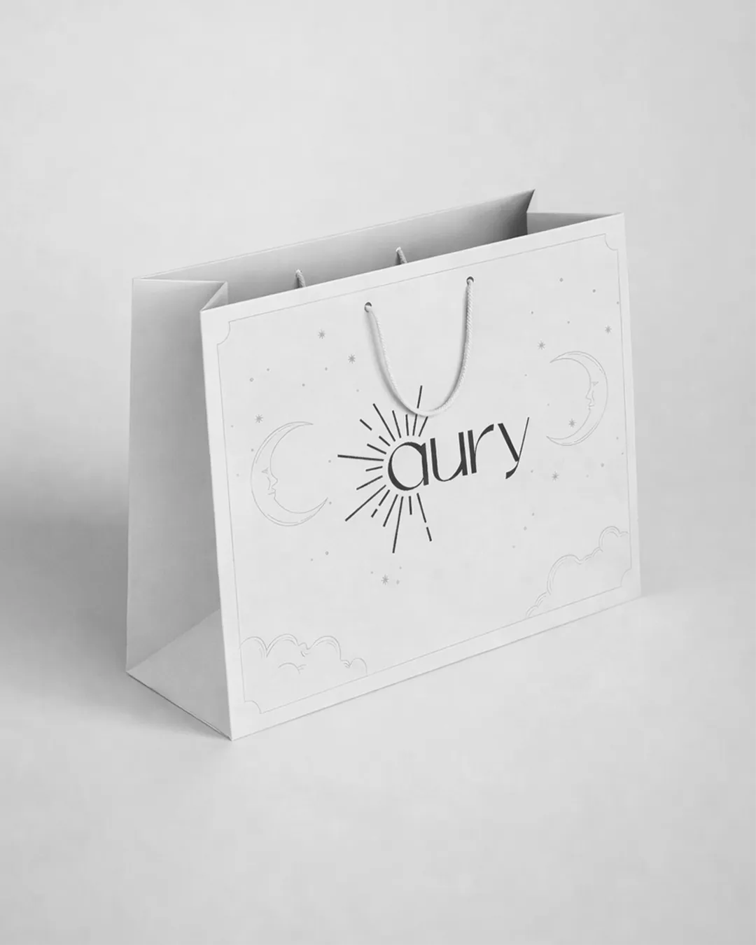 Bolsa de papel blanca con el logo de Aury y detalles gráficos de la identidad visual